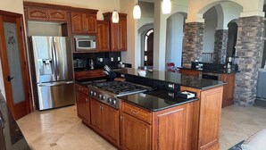 A kitchen with wooden cabinets, a stainless steel refrigerator, a microwave, a stove, and a stone accent wall. - Peaceful Monument Retreat (San José del Cabo)