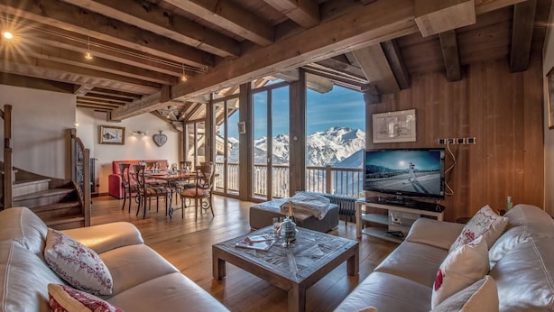 A spacious living area with a wooden ceiling, a sofa set, a coffee table, a TV, and a dining area with a mountain view. - La Forêt du Praz (Courchevel)