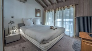 A bedroom with a large bed, a bedside lamp, a framed picture on the wall, and a window with curtains. - La Forêt du Praz (Courchevel)