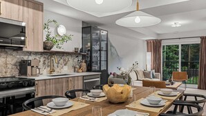 Une cuisine moderne avec un coin repas, des meubles en bois, une cuisinière encastrée et une grande table en bois dressée pour le repas.