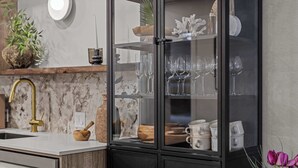 Une cuisine dotée d’un plan de travail en marbre, d’un robinet doré, d’un meuble noir aux portes en verre et d’une plante en pot.