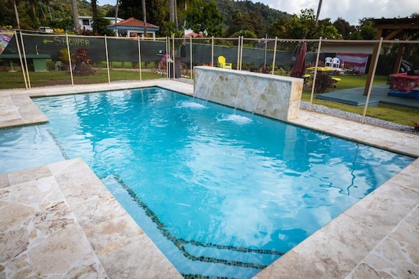 A rectangular swimming pool with a stone border and a small waterfall feature.