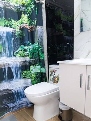 A bathroom with a toilet, a sink, and a shower curtain depicting a waterfall.