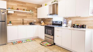 A modern kitchen with white cabinets, a stainless steel refrigerator, a built-in oven, and a coffee station. - Beach & Rainforest House with Private Pool (Rio Grande)