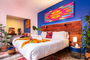 A hotel room with a large bed, a wooden headboard, a colorful abstract painting, and a potted plant. - Condesa 7-suite villa · hot tub & pool table (Mexico City)