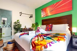 Une chambre d’hôtel avec un lit, une table de chevet, un miroir et un mur vert orné d’une œuvre d’art colorée.