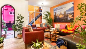 A living room with a red sofa, a coffee table, and a large painting of a cityscape. - Condesa 7-suite villa · hot tub & pool table (Mexico City)
