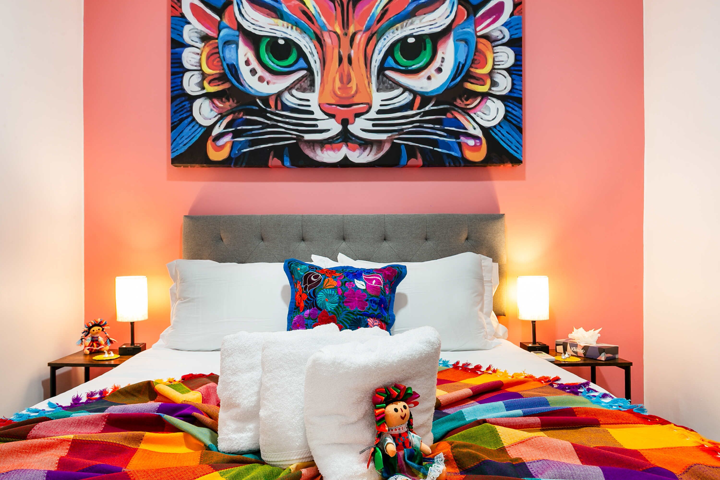 Une chambre d’hôtel avec un grand tableau représentant un tigre au mur, un lit avec du linge de maison blanc, des couvertures colorées et un coussin décoratif.