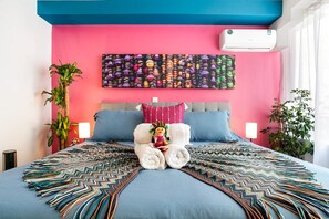 A bed with a colorful blanket, a decorative pillow, and a wall-mounted air conditioner. - Quiet-Street Condesa 3BR, 2 Kings, Balconies & AC (Mexico City)