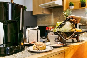 A kitchen counter with a coffee maker, a plate with a pastry, a glass of water, and a hand pouring a drink from a pitcher. - Quiet-Street Condesa 3BR, 2 Kings, Balconies & AC (Mexico City)