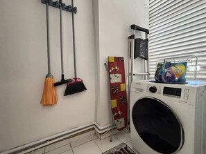 Ein Waschbereich mit Waschmaschine, einem Mop, einer Bürste und einem Wäschekorb.