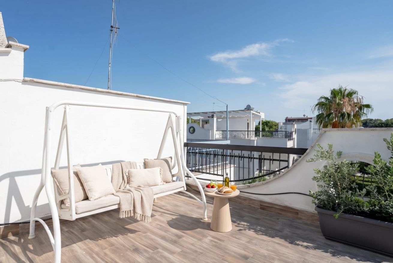 Eine Dachterrasse mit einer weißen Couch, einem kleinen Tisch mit Getränken und Blick auf die Nachbargebäude.
