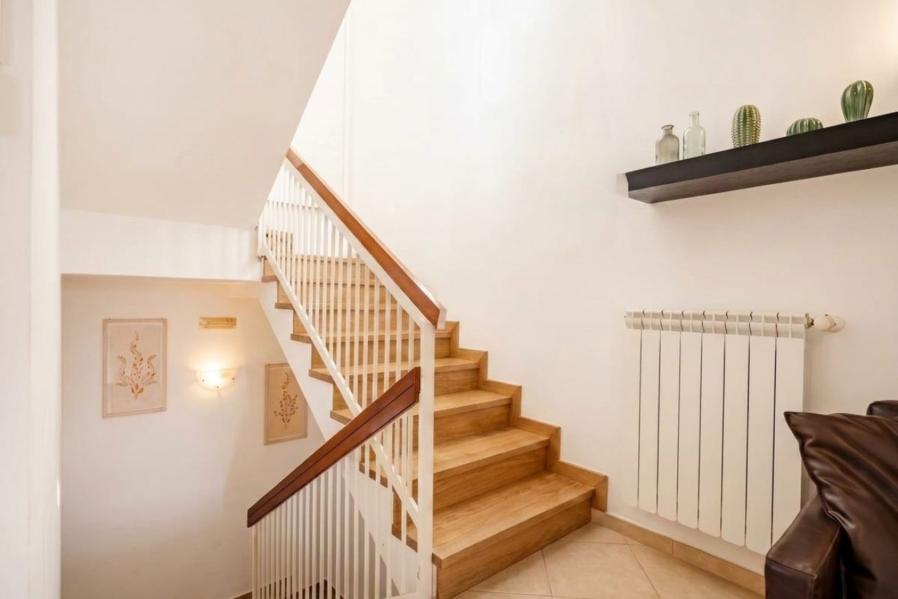 Una scala con gradini in legno e ringhiere bianche, un termosifone e una mensola con oggetti decorativi.