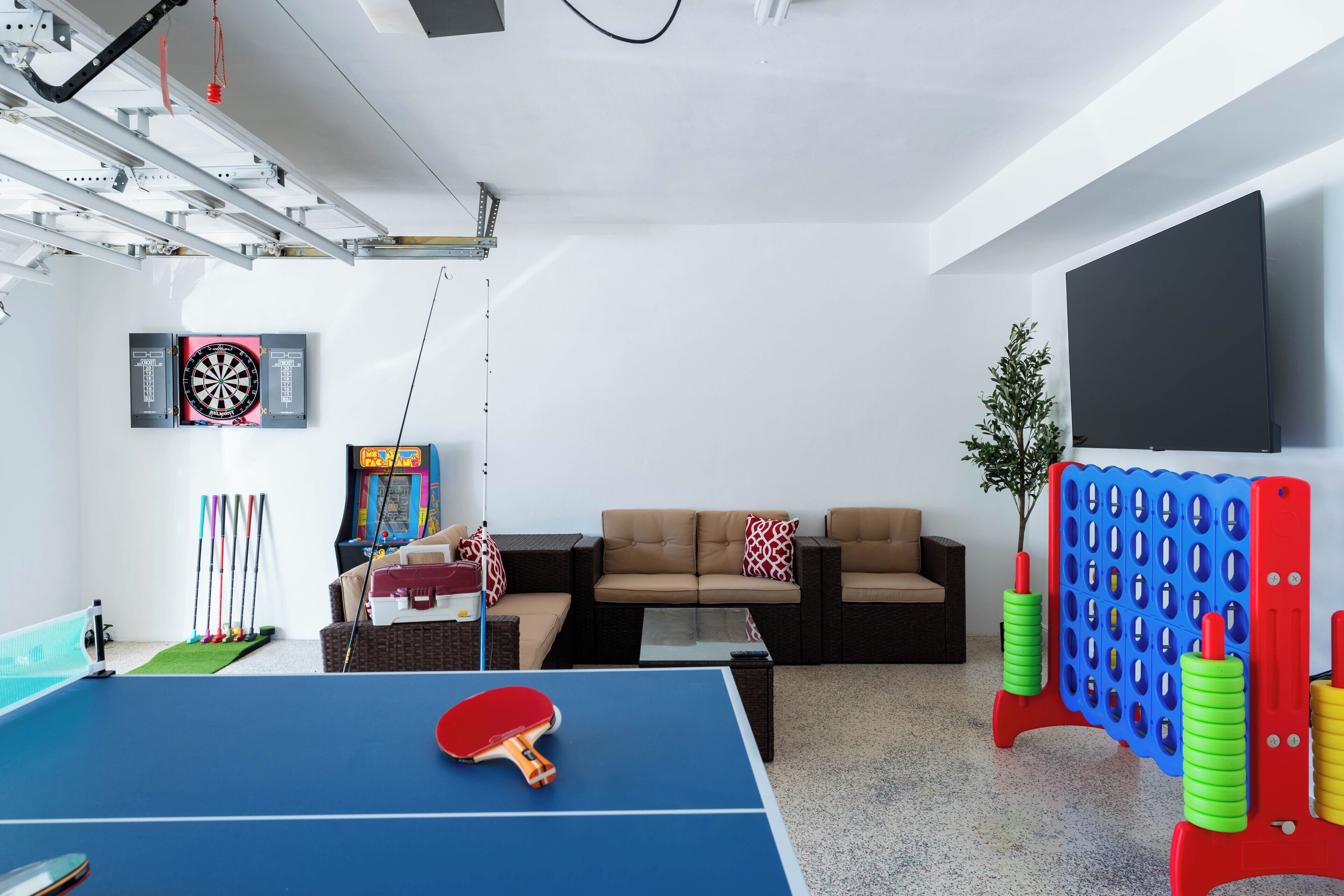 A room with a ping pong table, a dartboard, and a foosball table.