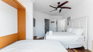 Quarto de hotel com uma cama grande, um ventilador de teto e uma cabeceira de madeira.