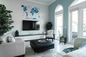 Un saló modern amb un mapa del món, una televisió de pantalla plana, un sofà, una cadira i una zona de menjador amb una taula.