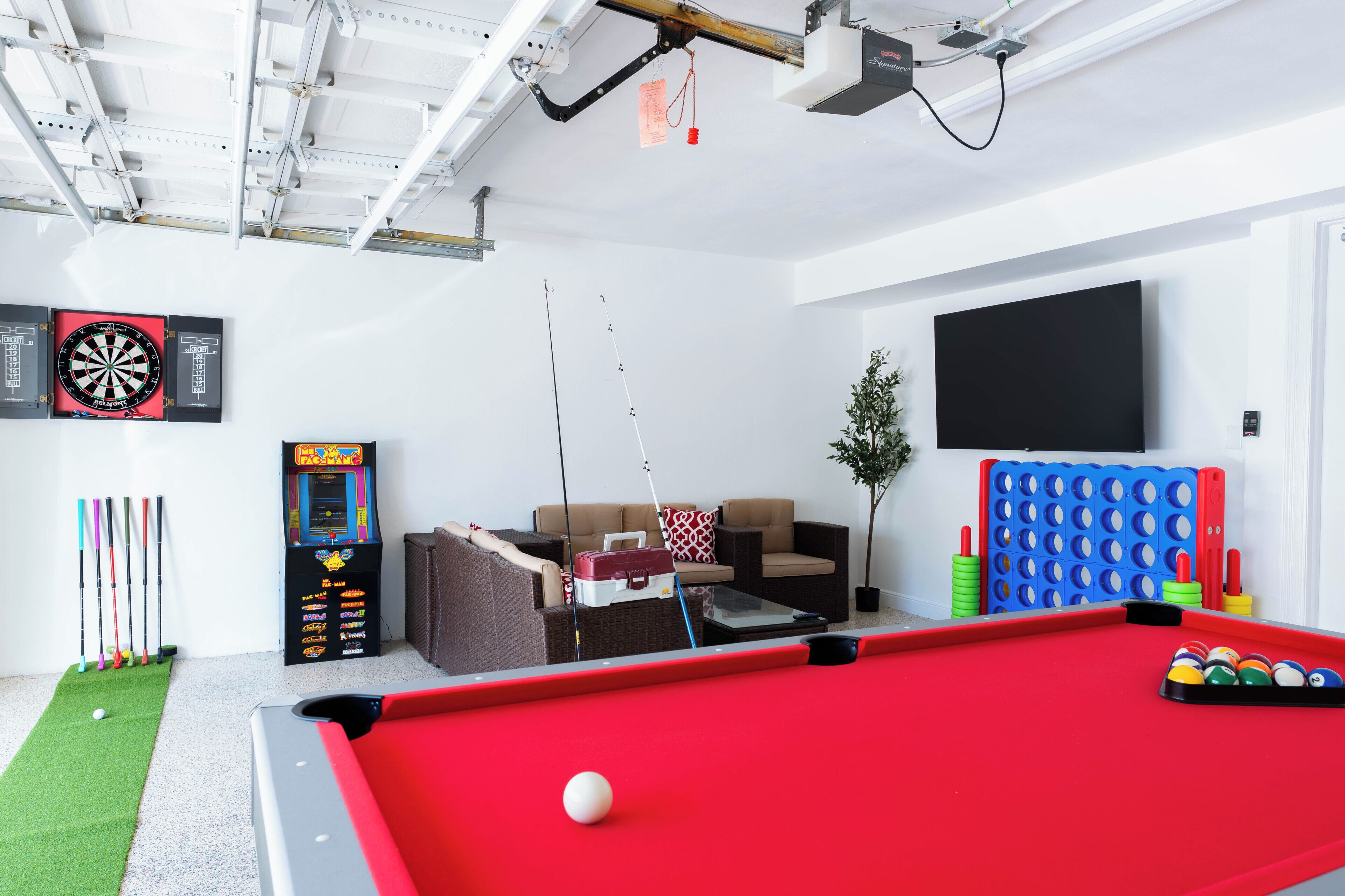 A recreational room with a pool table, darts, a fishing rod, and a gaming machine.