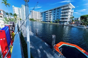 Blick auf das Wasser mit einer Anlegestelle, einem Boot und modernen Gebäuden im Hintergrund.