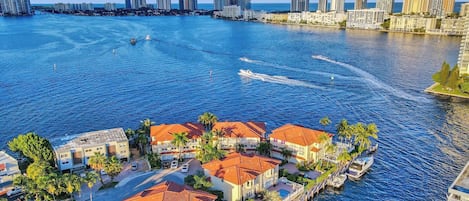 A coastal area with a marina, buildings with red roofs, and a city skyline in the background.