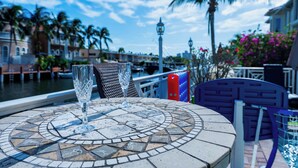 Uma mesa com dois copos transparentes, um pátio com azulejos, vista para um canal com edifícios e uma palmeira.