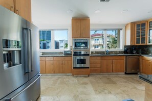A modern kitchen with stainless steel appliances, wooden cabinets, and a view of buildings through the windows. - Luxury Waterfront W/ Heated Pool & Canal Views! (North Miami Beach)