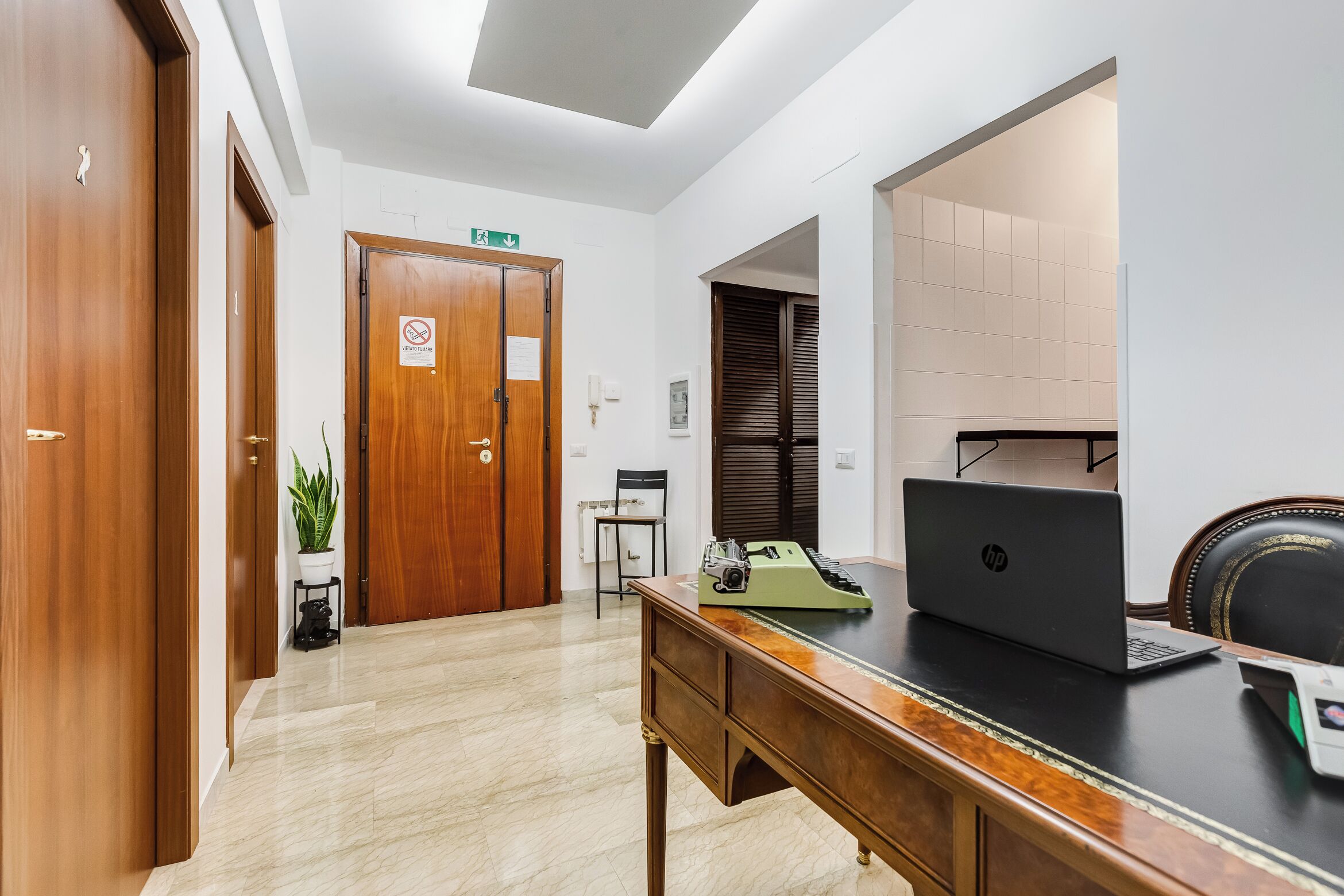 Een hotel lobby met houten deuren, een bureau met een HP laptop, een telefoon en een kamerplant.