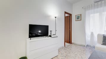 Una sala moderna con una televisión de pantalla plana, una lámpara de pie, un sofá y una puerta que da a otra habitación.