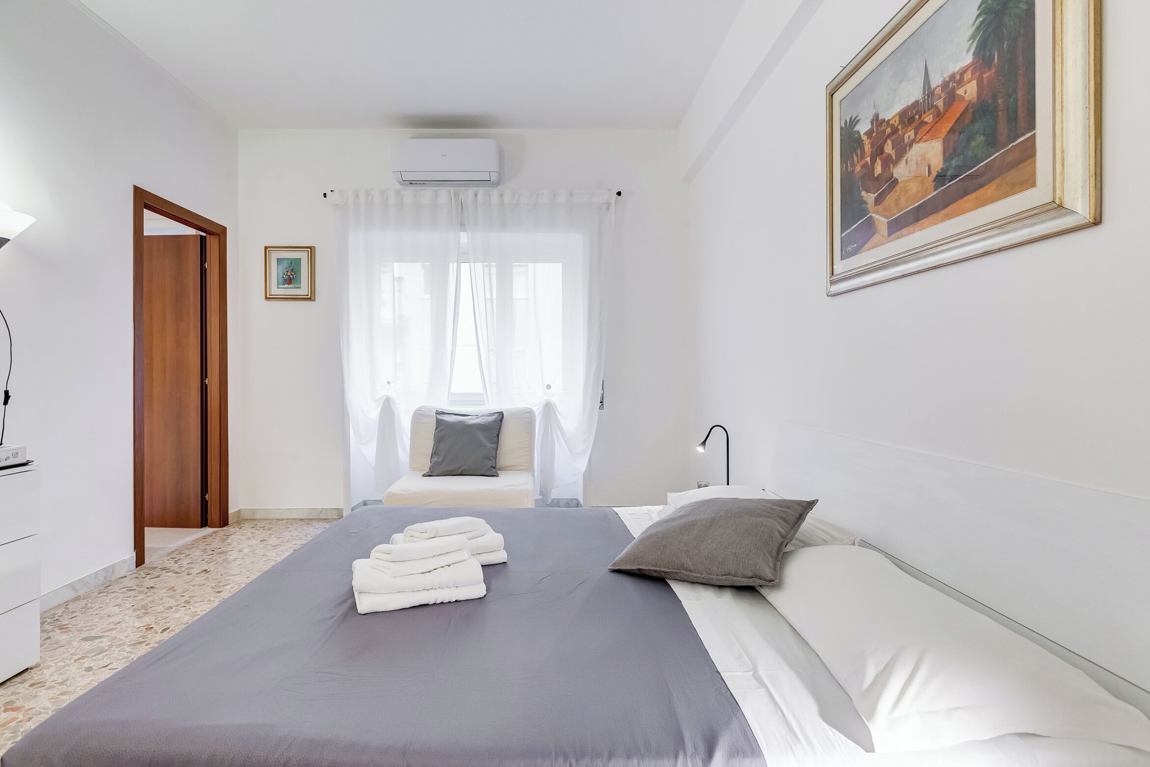 Une chambre d’hôtel avec un lit, une table de chevet, une lampe, un tableau au mur et un appareil de climatisation.