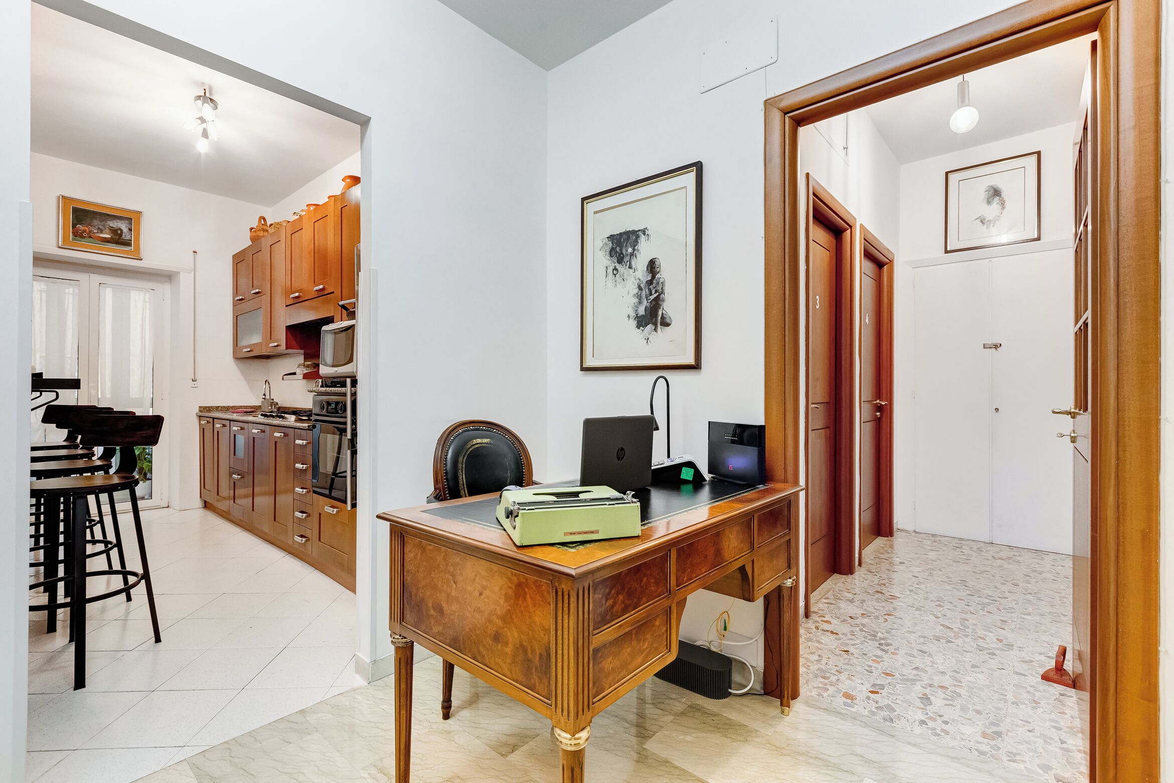 Une pièce avec un bureau en bois, une chaise, un ordinateur portable et un tableau encadré accroché au mur.