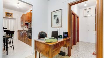 Een kamer met een houten bureau, een stoel, een laptop en een ingelijst schilderij aan de muur.