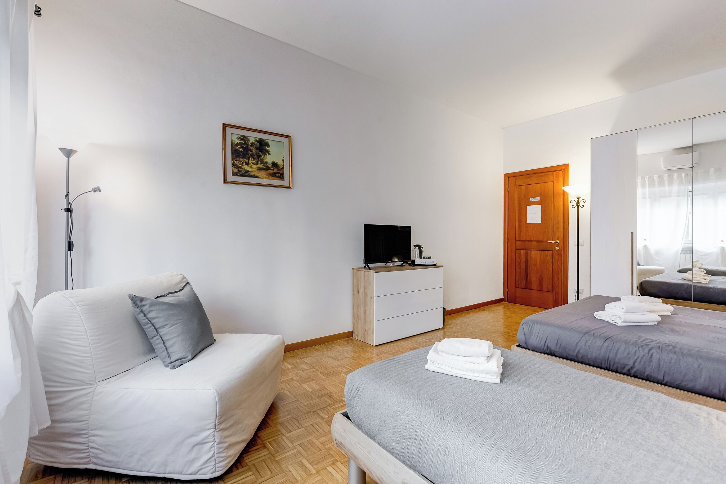 Une chambre d’hôtel avec un lit, un canapé, une télévision, une commode et une porte.