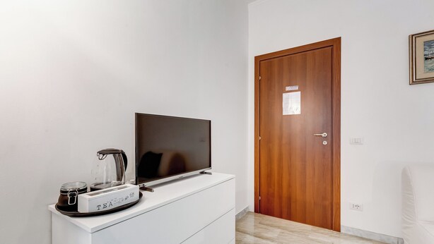 A room with a white dresser, a flat-screen TV, a coffee maker, and a wooden door.