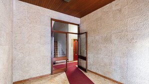 A hallway with a red carpet, a wooden ceiling, and a textured wall.