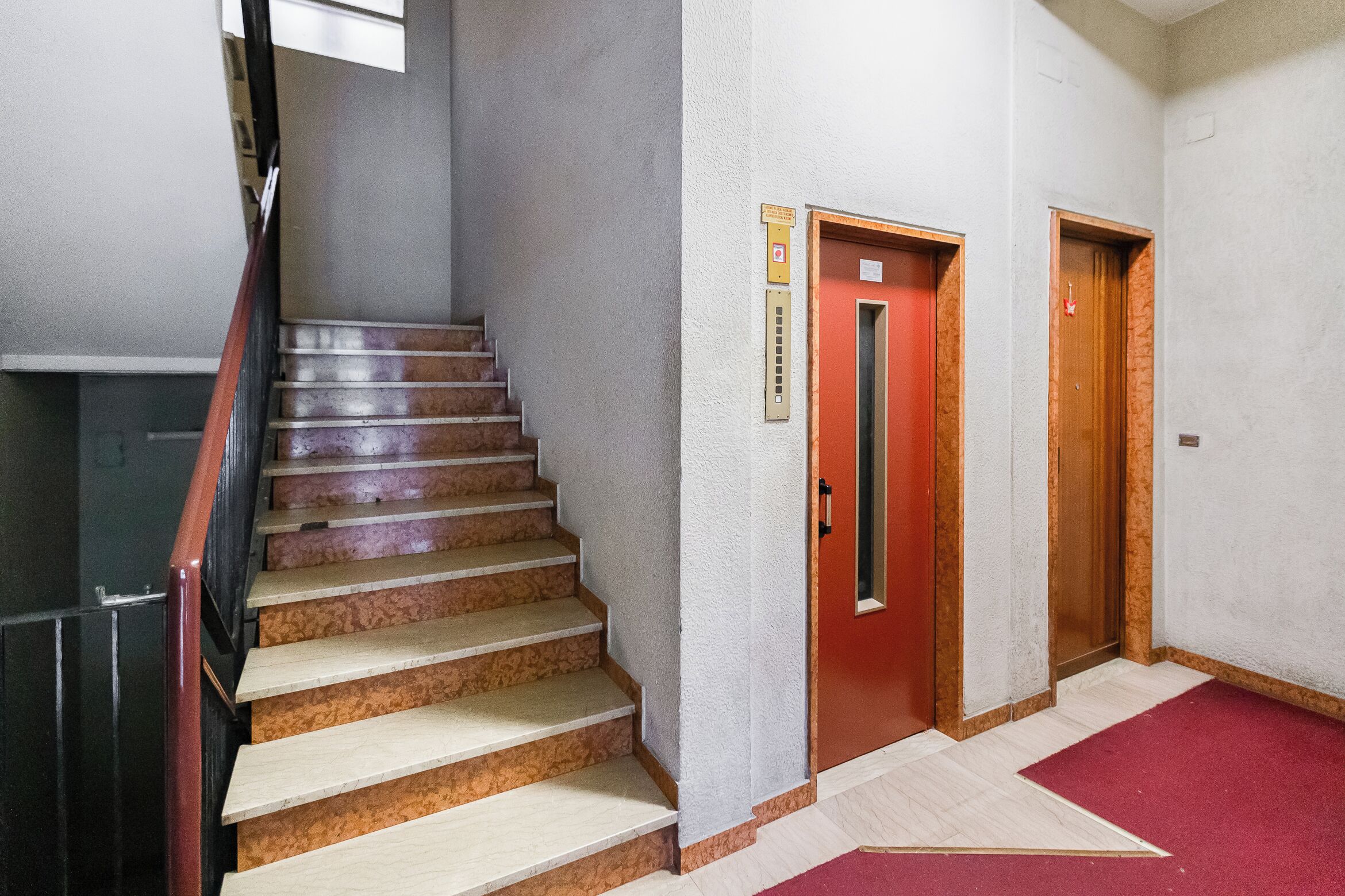 Eine Treppe mit Holzboden und einem roten Teppich, der zu einer Tür mit rotem Griff führt.