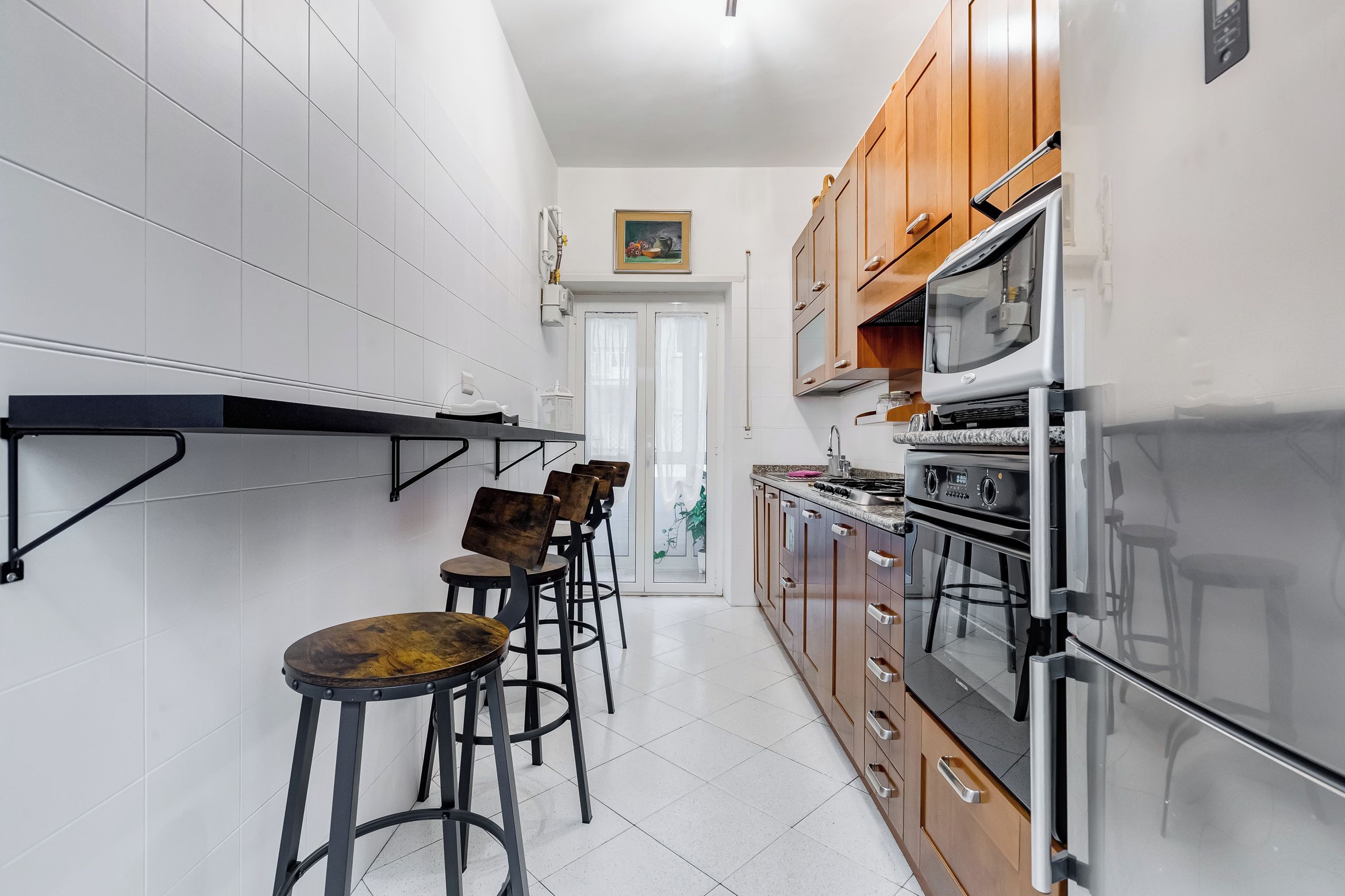 Une cuisine équipée d’un four encastré, d’un four à micro-ondes et d’une cuisinière. On y trouve également des tabourets de bar et une étagère suspendue.