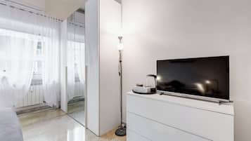 Une chambre d’hôtel moderne, équipée d’un lit, d’un téléviseur à écran plat fixé à une armoire blanche, d’une lampe sur pied et d’un grand miroir qui reflète la pièce.