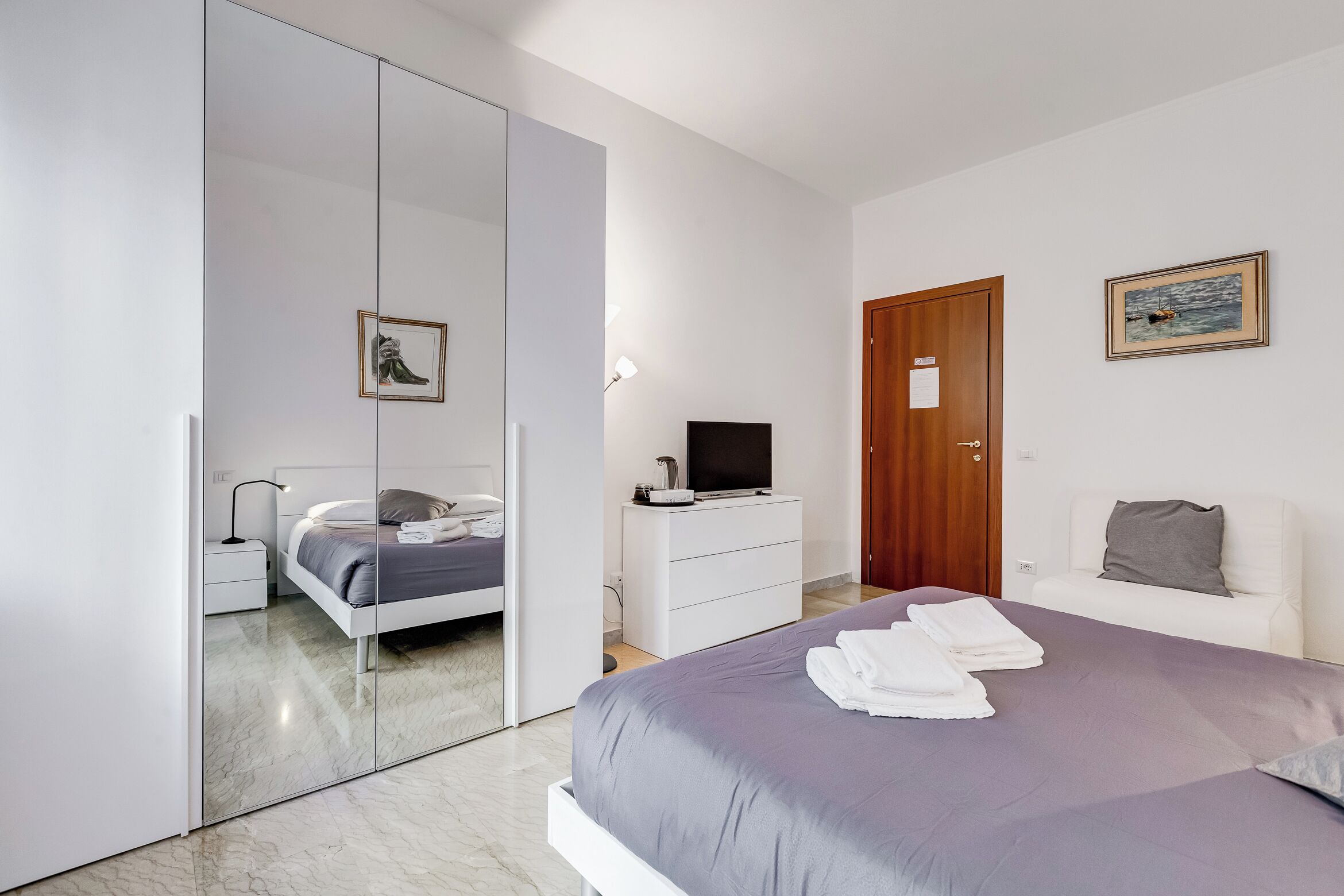 A modern bedroom with a bed, a TV, a desk, and a wardrobe.
