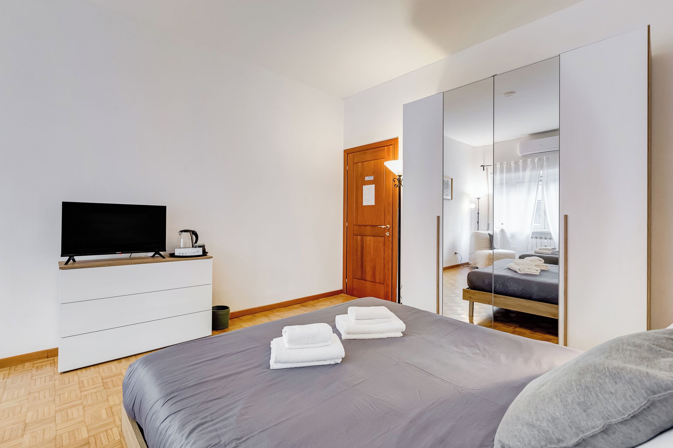 A modern hotel room with a bed, a TV, a wardrobe, and a mirror.