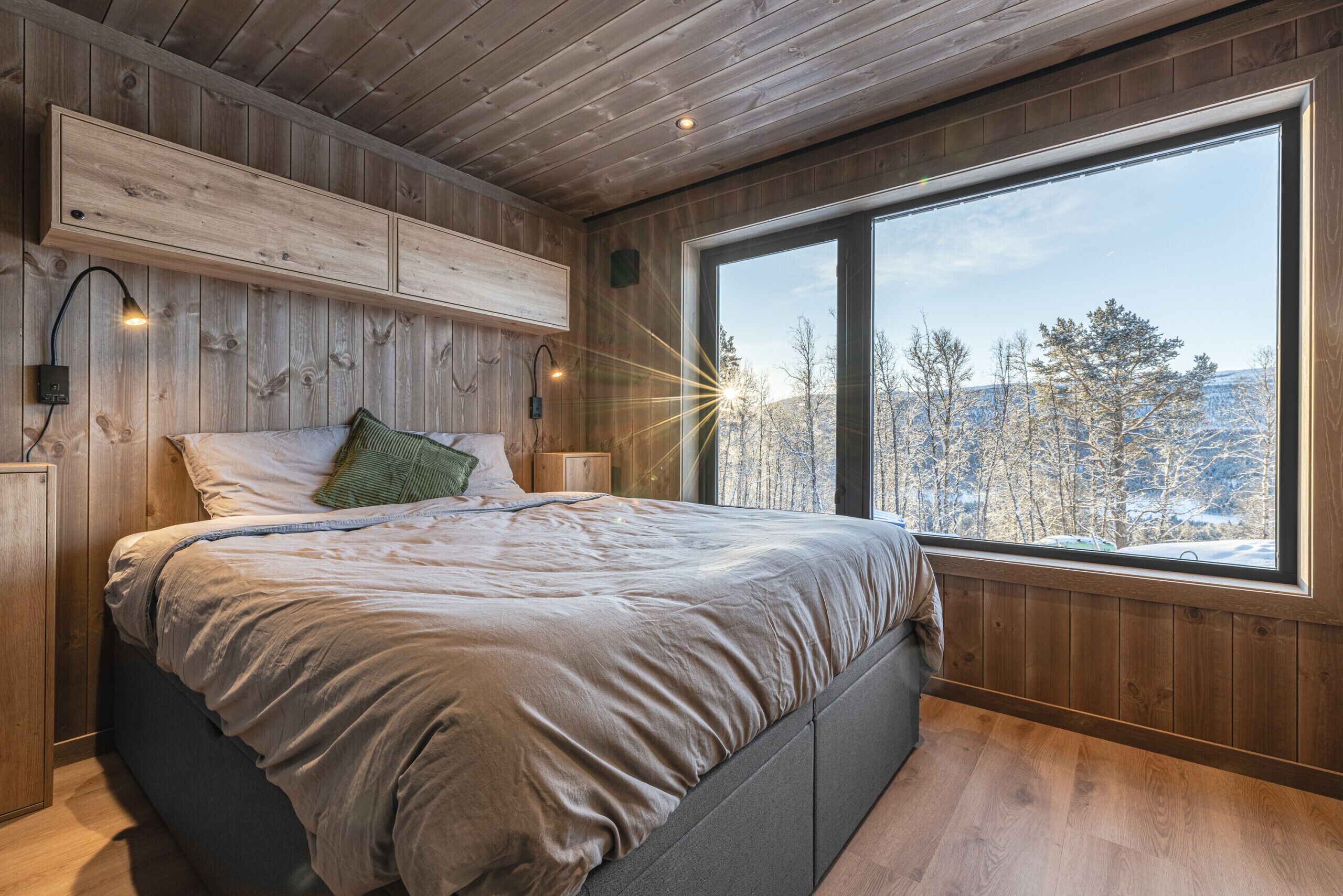Ein Schlafzimmer mit großem Fenster, Holzwänden und einem Bett mit einem grünen Kissen.