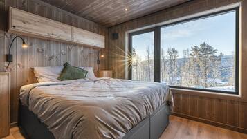 Ein Schlafzimmer mit großem Fenster, Holzwänden und einem Bett mit einem grünen Kissen.