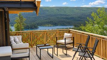 Eine Holzterrasse mit Gartenmöbeln, einem Pergola und einem schönen Blick auf einen See und einen Wald.