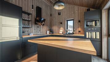 A modern kitchen with a large island, dark cabinetry, wooden walls, and a view of the outdoors.