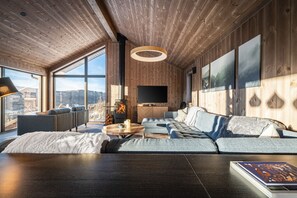 A modern living room with a large window, a fireplace, and a flat-screen TV. - New luxury cabin in Geilo with hot tub, mountain views & ski access (Hol)