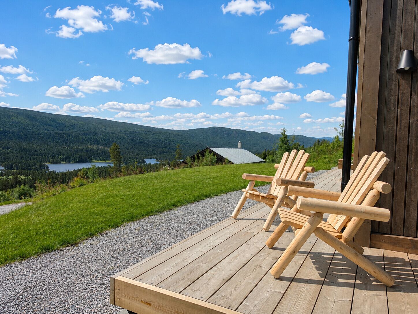 Een houten terras met twee Adirondack-stoelen, uitkijkend op een meer en bergen.