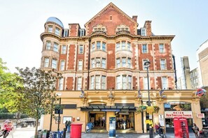 A historic building with a prominent corner turret, a ground-floor entrance with a sign for 'Queensway Station,' and a visible 'New Fortune Cookie' shop. - Stylish Boutique Studio in Notting Hill (London)