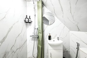 Ein Badezimmer mit weißer Marmorwand, einem grünen Duschvorhang, einem Waschbecken mit Spiegel und zwei Flaschen an der Wand.