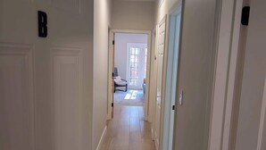 Un couloir avec des portes blanches, un luminaire et une chaise au loin.