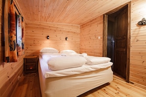 A wooden cabin room with a bed, a nightstand, and a door.