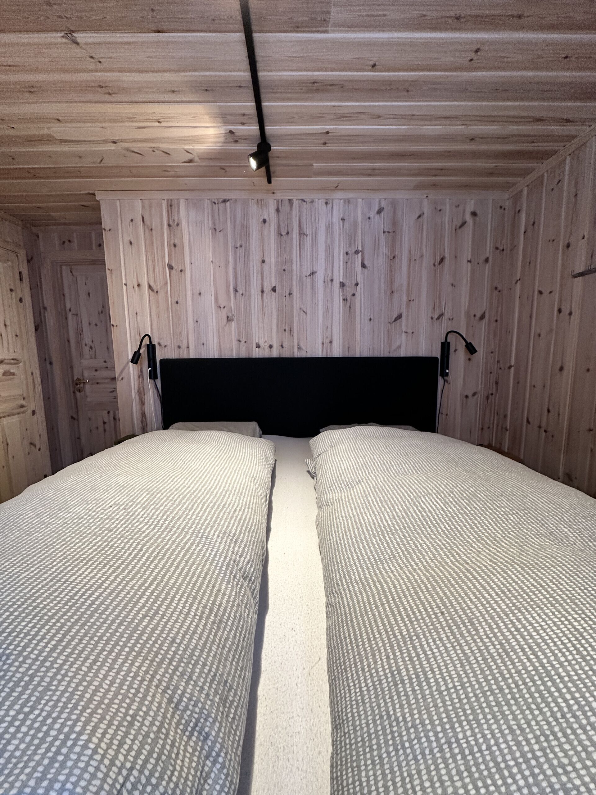 A room with a wooden ceiling, two beds with white bedding, and a black headboard.