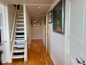 A hallway with a wooden staircase, wooden flooring, and framed artwork on the walls.